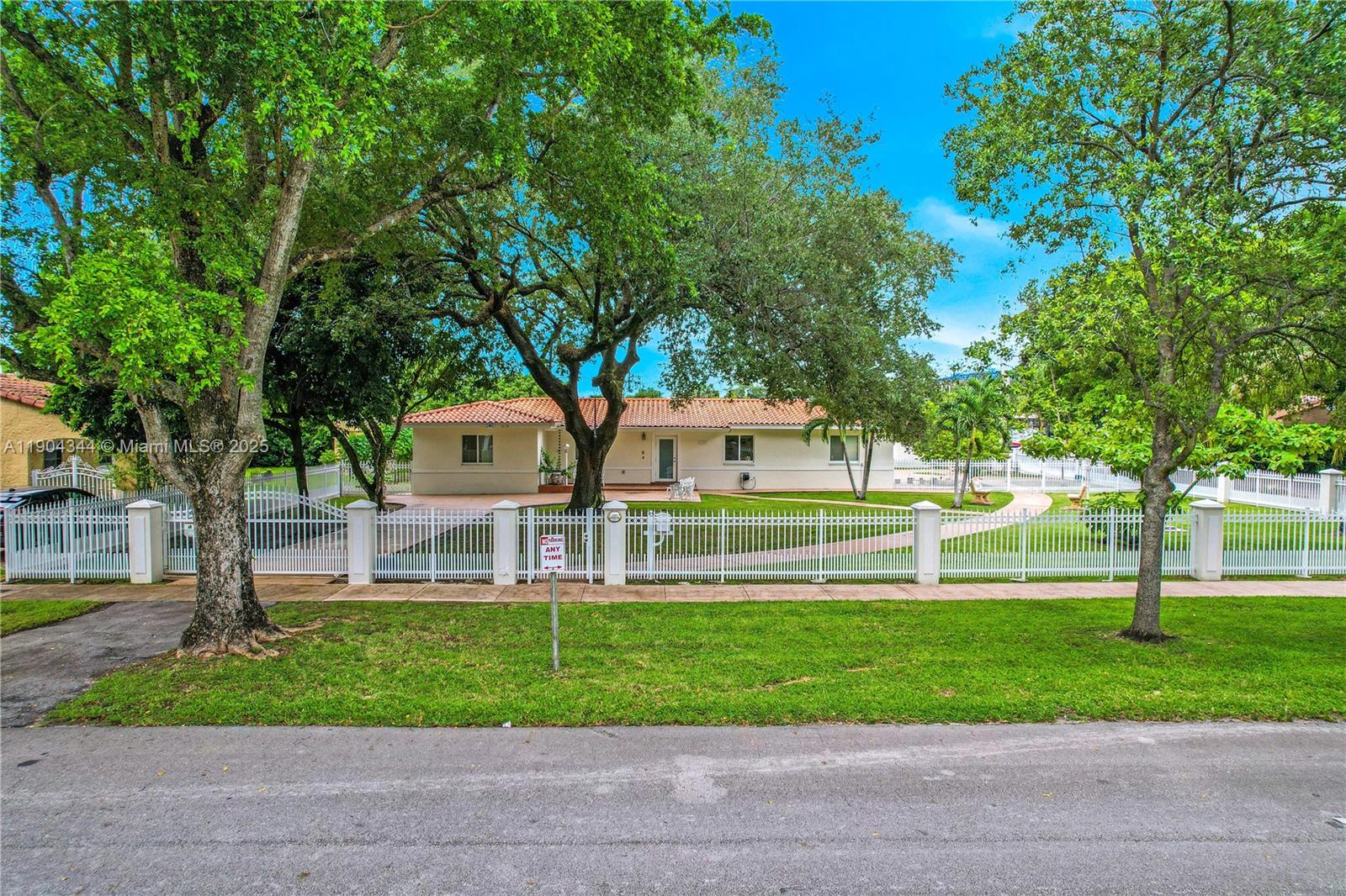 A single-story house with a tiled roof sits behind a white picket fence and trees — 1407 San Marco Ave, Coral Gables FL 33134, CORAL GABLES, FL