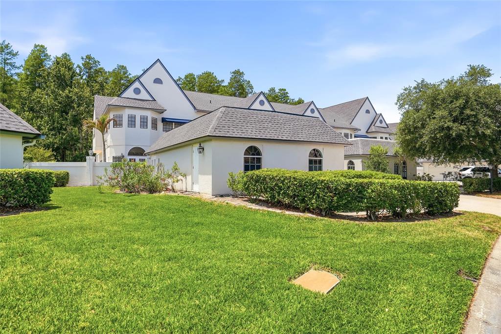 A white house with a gray shingled roof sits behind a manicured green lawn — 18740 WIMBLEDON CIRCLE, LUTZ, FL