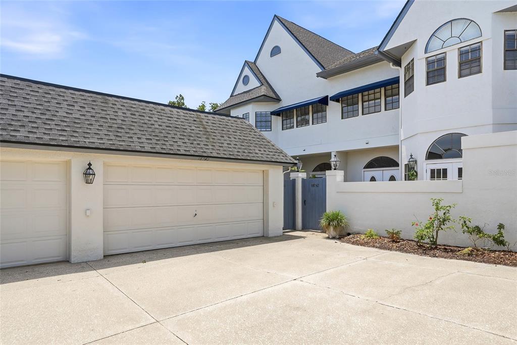 A white multi-story house features a detached garage and a gated courtyard entrance — 18740 WIMBLEDON CIRCLE, LUTZ, FL