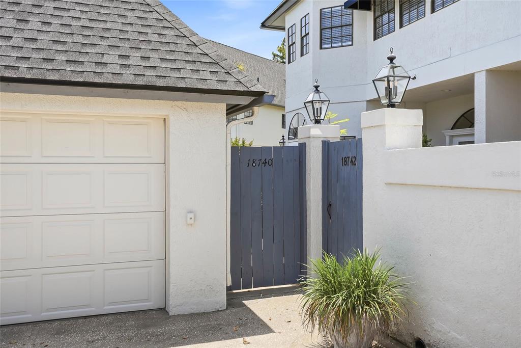 A white stucco exterior features a garage, a blue wooden gate, and two outdoor lanterns — 18740 WIMBLEDON CIRCLE, LUTZ, FL
