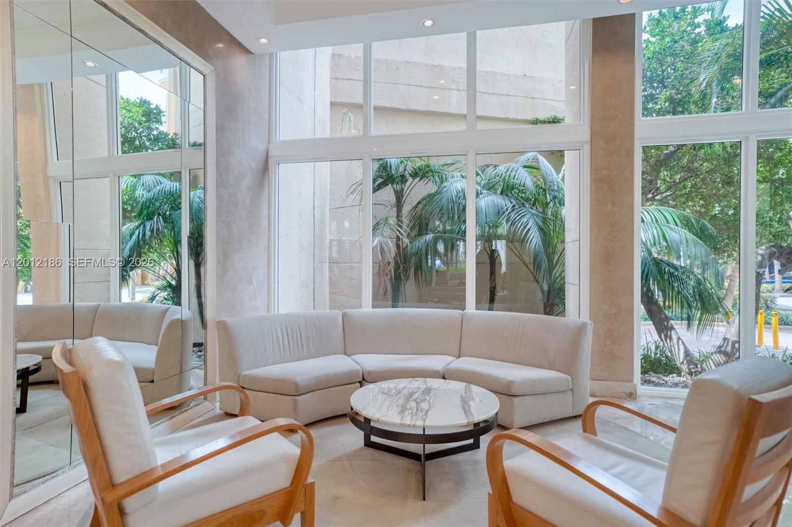 A seating area features a curved sofa, two wooden armchairs, and floor-to-ceiling windows overlooking palms — 770 Claughton Island Dr # 1114, Miami FL 33131, MIAMI, FL