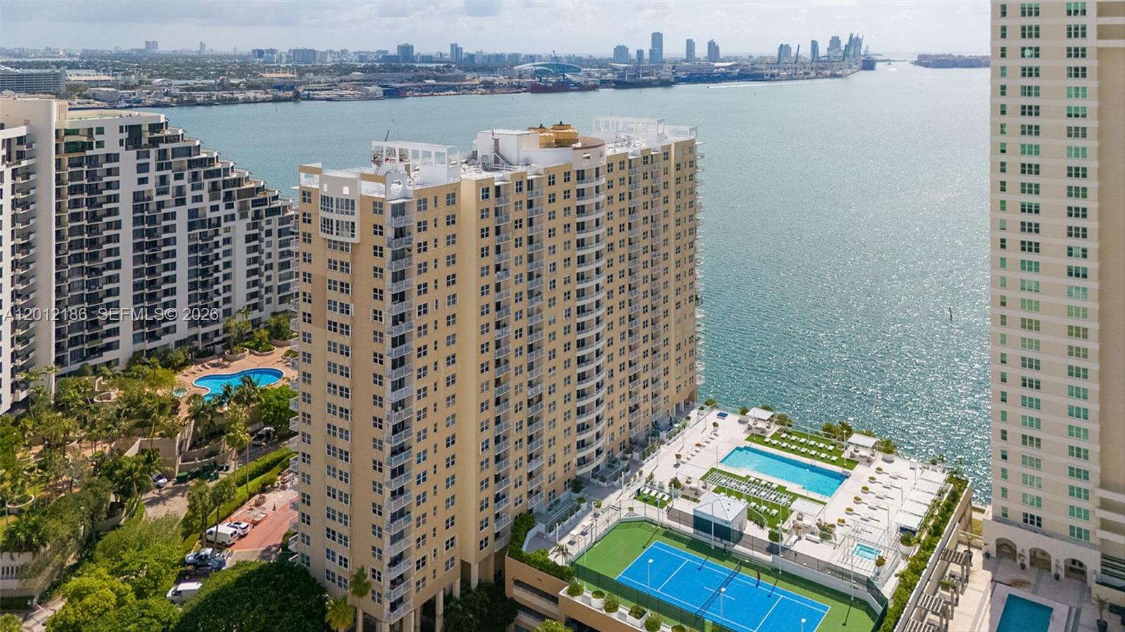 An aerial view shows a tall tan residential building with a pool and tennis court — 770 Claughton Island Dr # 1114, Miami FL 33131, MIAMI, FL