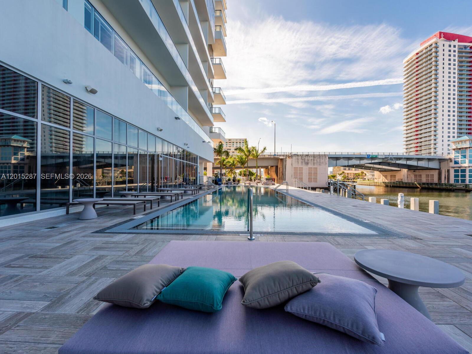 A swimming pool sits on a patio next to a modern building and a bridge — 4010 S Ocean Dr # R2004, Hollywood FL 33019, HOLLYWOOD, FL