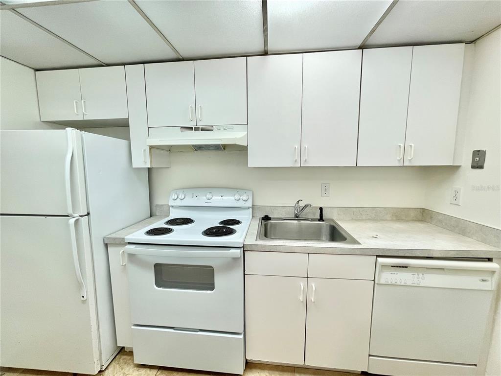 A kitchen features white cabinets, white appliances, a stainless steel sink, and laminate countertops — 719 SW 75TH STREET UNIT 103, GAINESVILLE, FL