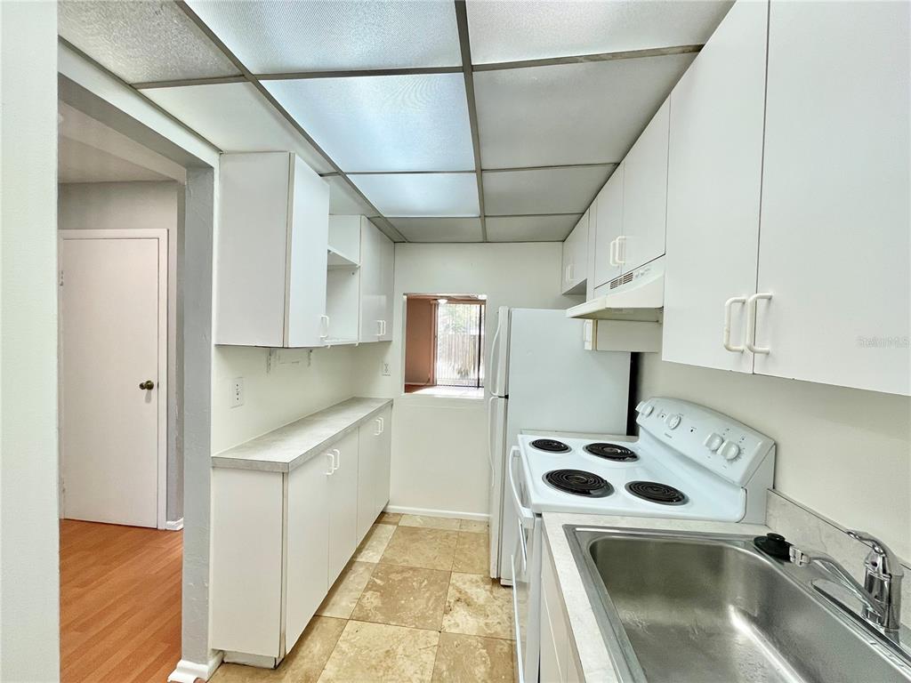 A galley kitchen features white cabinets, a white stove, a sink, and tiled flooring — 719 SW 75TH STREET UNIT 103, GAINESVILLE, FL