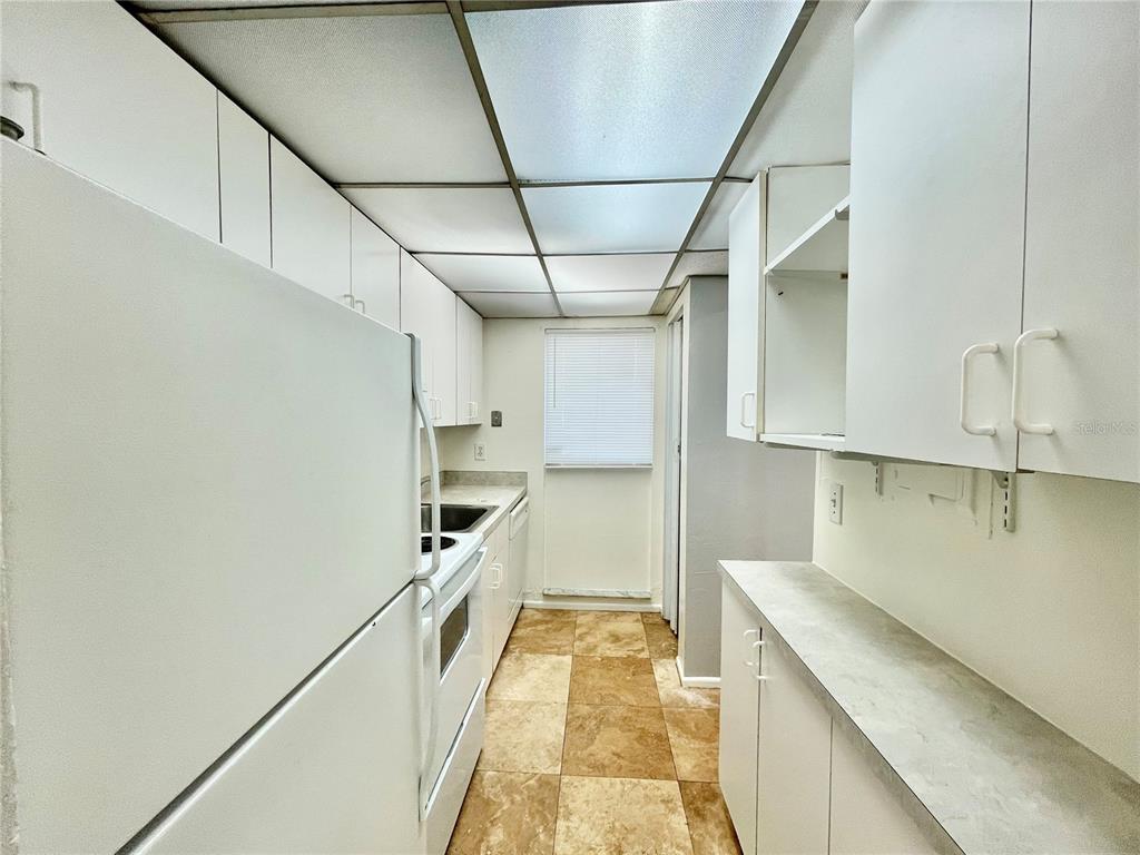 A galley kitchen features white cabinets, white appliances, tiled floors, and a drop ceiling — 719 SW 75TH STREET UNIT 103, GAINESVILLE, FL