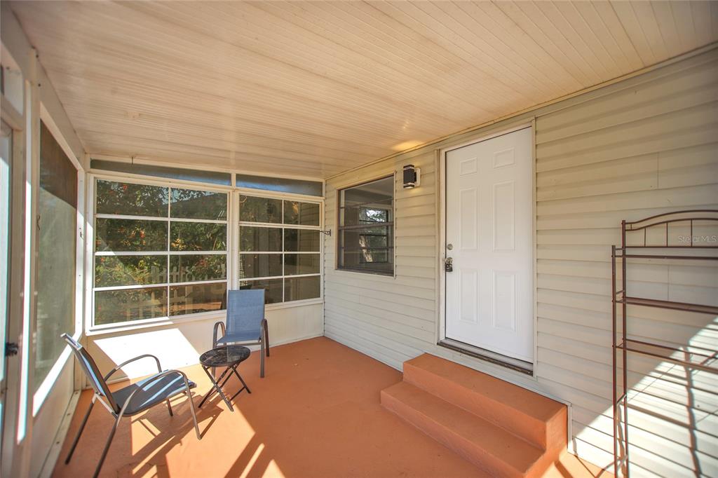 A screened-in porch features light-colored siding, a white door, and an orange concrete floor — 847 JASMINE AVENUE, HOLLY HILL, FL