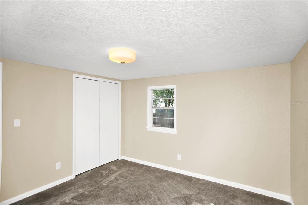 A bedroom with beige walls, gray carpet, a white closet, and a single window — 847 JASMINE AVENUE, HOLLY HILL, FL