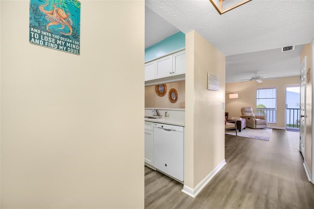 A view from a hallway looking into a kitchen and a living area with flooring — 260 MEDALLION BOULEVARD UNIT F, MADEIRA BEACH, FL
