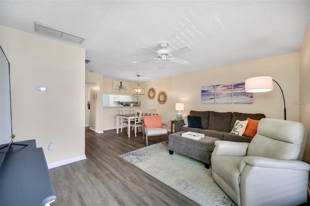 A living room with wood-look flooring, a gray sofa, and an adjacent dining area — 260 MEDALLION BOULEVARD UNIT F, MADEIRA BEACH, FL