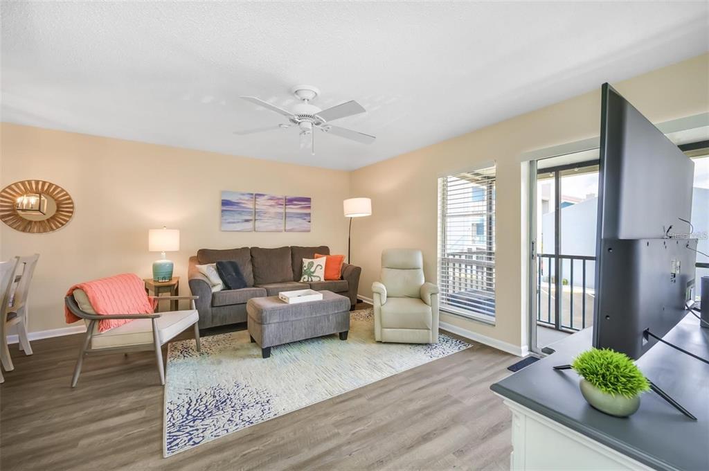 A living room features a gray sofa, an armchair, a television, and a sliding glass door — 260 MEDALLION BOULEVARD UNIT F, MADEIRA BEACH, FL