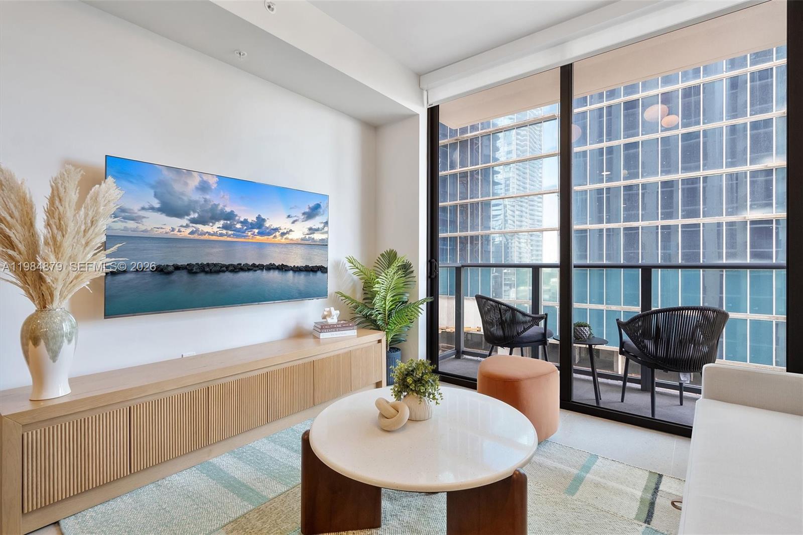 A modern living room features a wall-mounted television, light wood media console, and balcony access — 11 NE 6th St # 1805, Miami FL 33132, MIAMI, FL