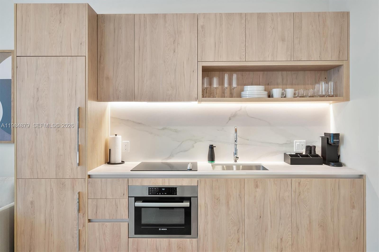 A modern kitchenette features light wood cabinetry, a marble backsplash, and stainless steel appliances — 11 NE 6th St # 1805, Miami FL 33132, MIAMI, FL