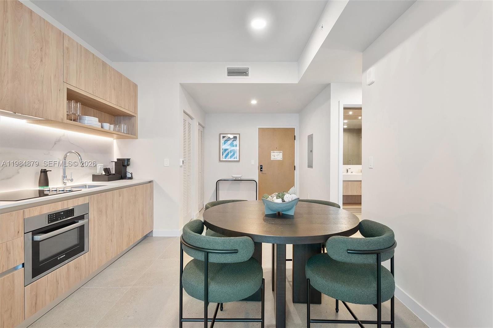 A modern kitchen features light wood cabinetry, a round dining table, and green upholstered chairs — 11 NE 6th St # 1805, Miami FL 33132, MIAMI, FL