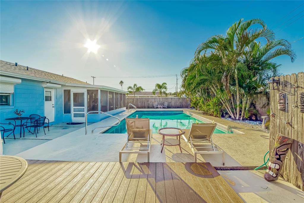 A backyard features a swimming pool, lounge chairs, a wooden deck, and a blue house — 6004 GOLF AND SEA BOULEVARD, APOLLO BEACH, FL