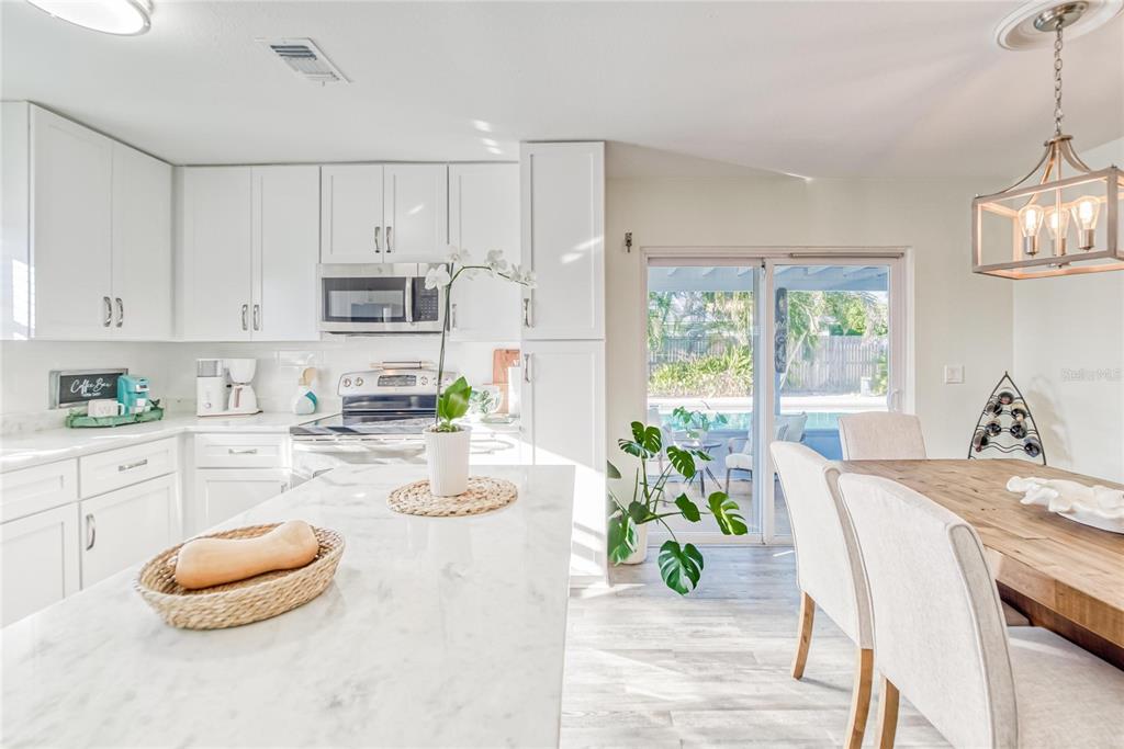 A bright kitchen features white cabinetry, a marble-topped island, and a dining area with patio access — 6004 GOLF AND SEA BOULEVARD, APOLLO BEACH, FL
