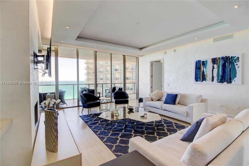 A modern living room features a white sofa, blue accent chairs, and floor-to-ceiling windows — 9705 Collins Ave # 1003N, Bal Harbour FL 33154, BAL HARBOUR, FL