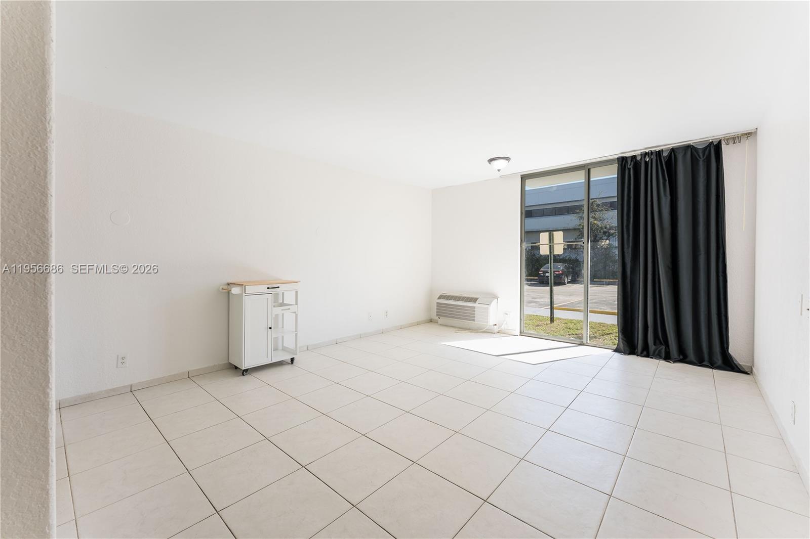 An empty room features white tiled floors, white walls, a small kitchen cart, and sliding doors — 16450 NW 2nd Ave # 103, Miami FL 33169, MIAMI, FL