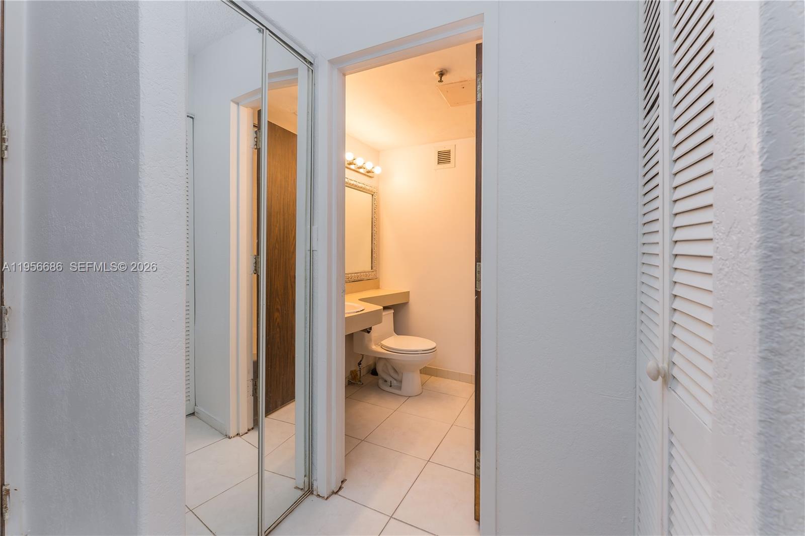 A bathroom with a toilet and vanity is visible through a doorway with mirrored doors — 16450 NW 2nd Ave # 103, Miami FL 33169, MIAMI, FL