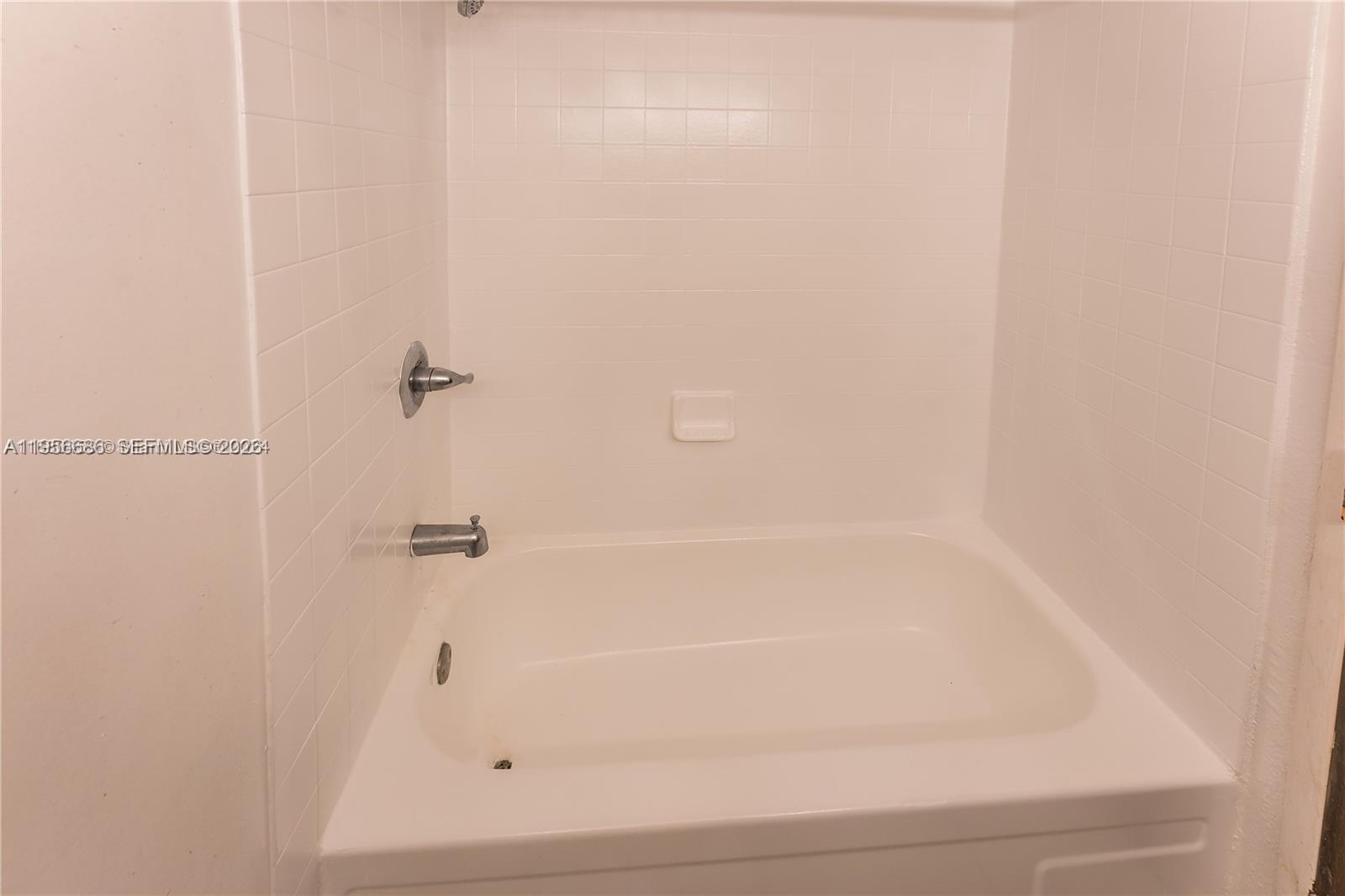 A white bathtub with a shower head and tiled walls in a bathroom — 16450 NW 2nd Ave # 103, Miami FL 33169, MIAMI, FL