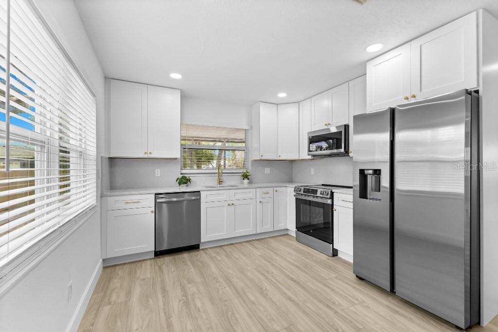 A kitchen features white cabinets, stainless steel appliances, light wood-look flooring, and a window — 5690 25TH STREET CIRCLE E, BRADENTON, FL
