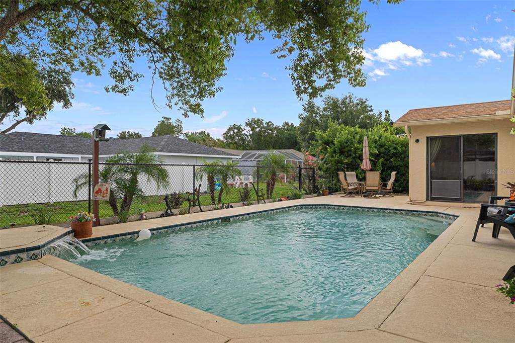 A backyard swimming pool with a water feature, patio furniture, and a chain-link fence — 8417 YEARLING LANE, NEW PORT RICHEY, FL