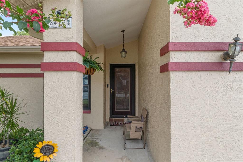 The front entryway features a covered porch with a door, a light fixture, and chairs — 8417 YEARLING LANE, NEW PORT RICHEY, FL