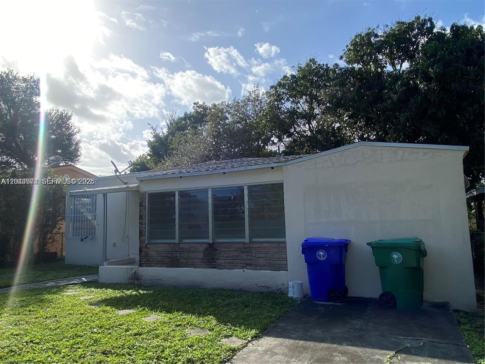 A single-story house exterior features a brick facade, jalousie windows, and two large trash bins — 170 NW 49th St, Miami FL 33127, MIAMI, FL