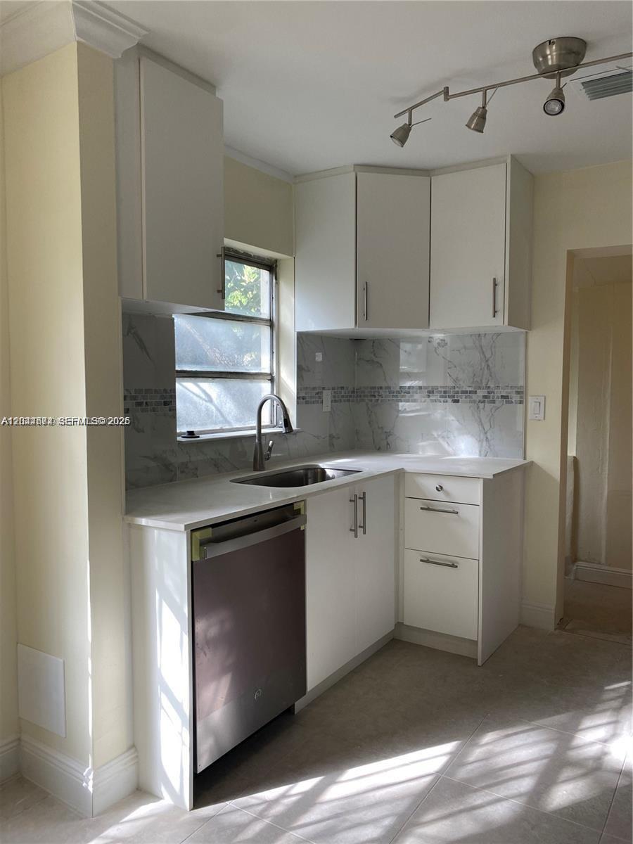 A small kitchen features white cabinets, a stainless steel dishwasher, and marble-patterned backsplash tiles — 170 NW 49th St, Miami FL 33127, MIAMI, FL