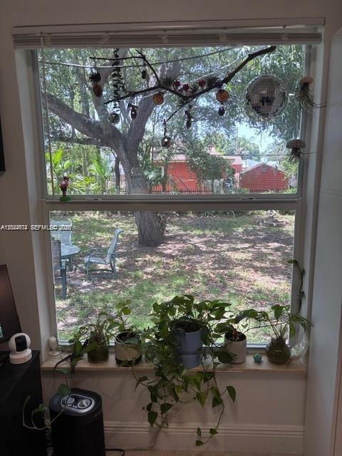 A window view shows a backyard with trees, a chair, and a table behind indoor plants — 170 NW 49th St, Miami FL 33127, MIAMI, FL