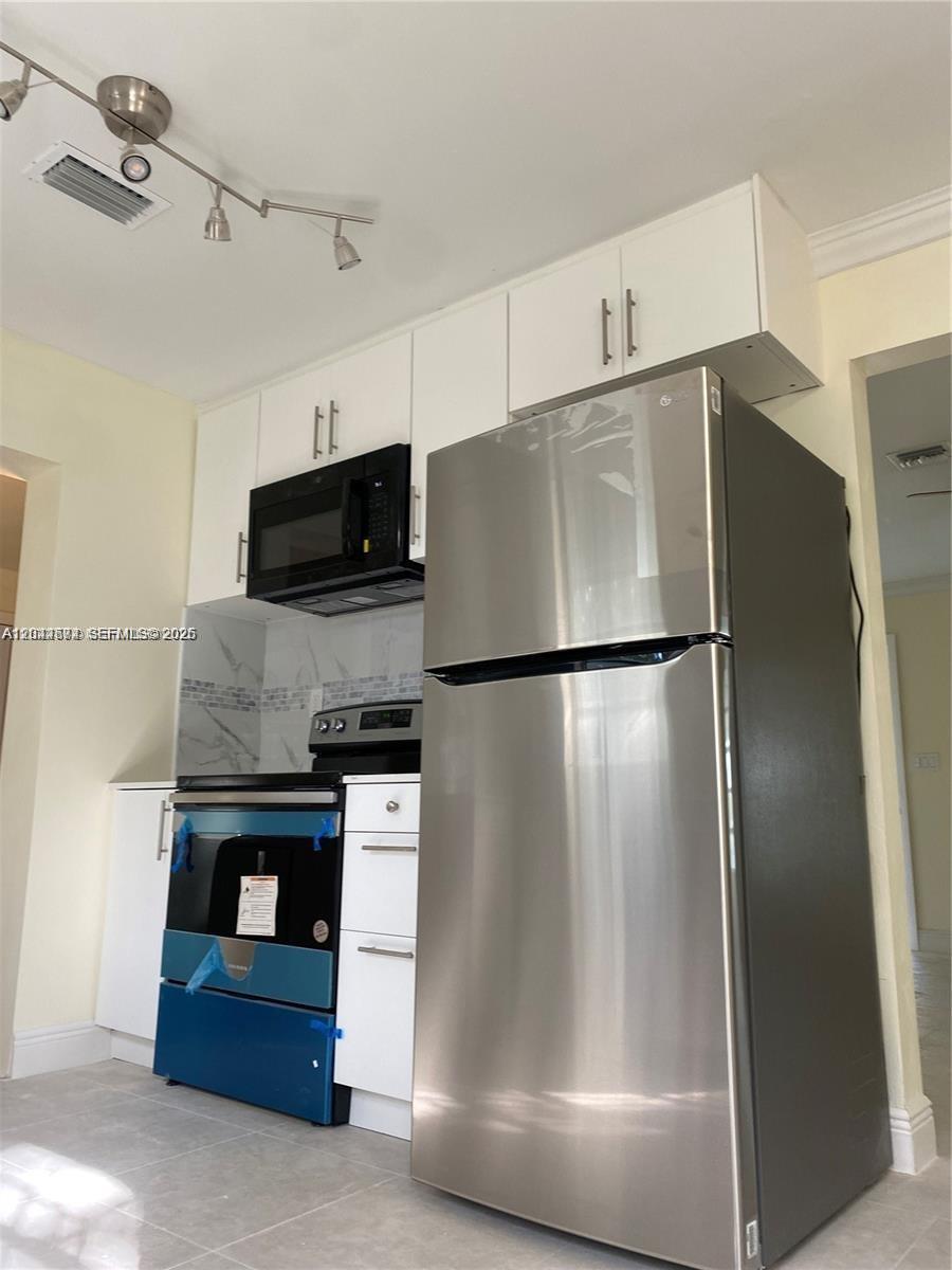 A kitchen features white cabinets, a stainless steel refrigerator, and a black range and microwave — 170 NW 49th St, Miami FL 33127, MIAMI, FL