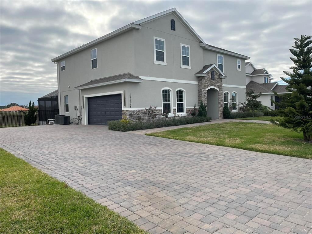 A two-story house with a gray stucco exterior, stone accents, and a paved driveway — 17708 SAWGRASS RUN, DEER ISLAND, FL