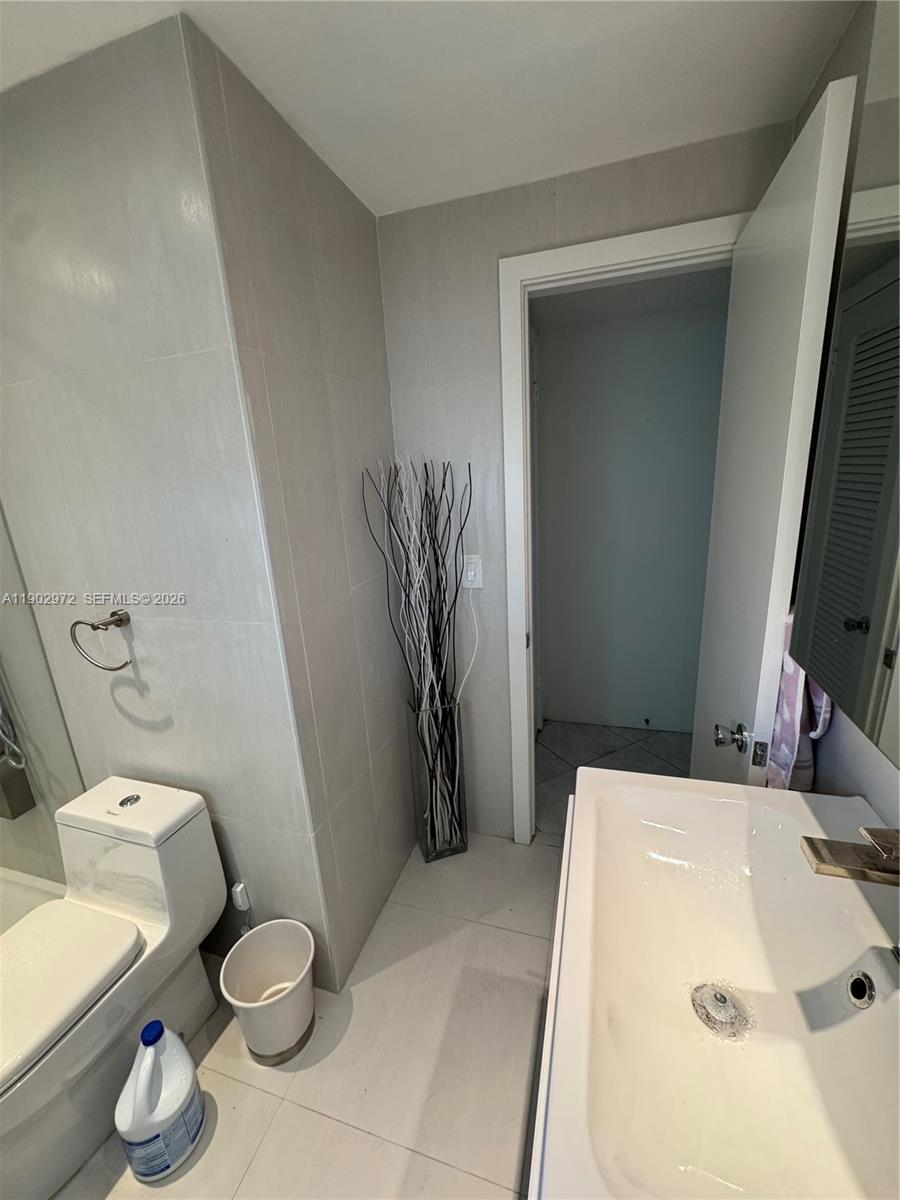 A modern bathroom features light gray tiled walls, a white pedestal sink, and a toilet — 1501 Arthur St # 1, Hollywood FL 33020, HOLLYWOOD, FL