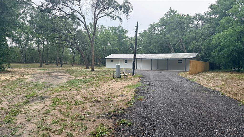 A white building with a metal roof and attached carport sits on a gravel driveway — 15535 LITTLE RANCH ROAD, SPRING HILL, FL