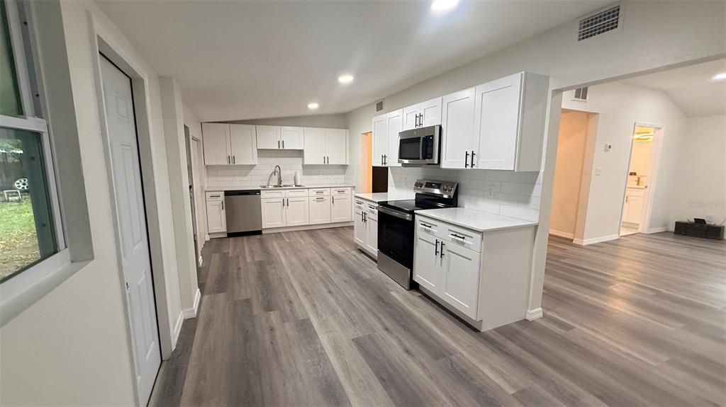 A kitchen features white cabinets, stainless steel appliances, and wood-look flooring — 15535 LITTLE RANCH ROAD, SPRING HILL, FL