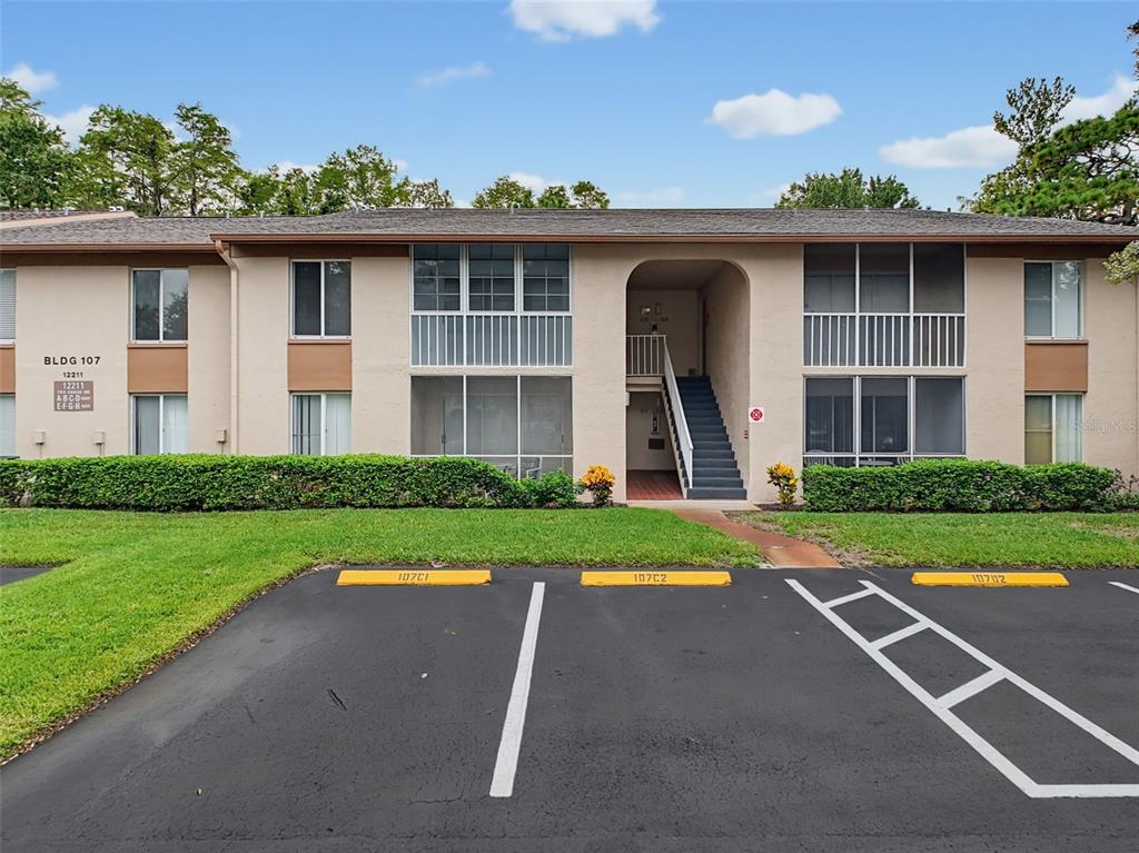 A two-story apartment building exterior with a central staircase and designated parking spaces in front — 12211 FOX CHASE DRIVE UNIT C1, HUDSON, FL