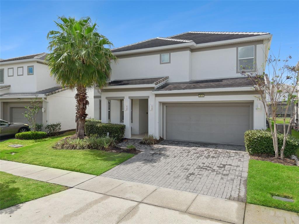 A two-story suburban house with a gray garage, paved driveway, and a palm tree — 2614 CALISTOGA AVENUE, KISSIMMEE, FL