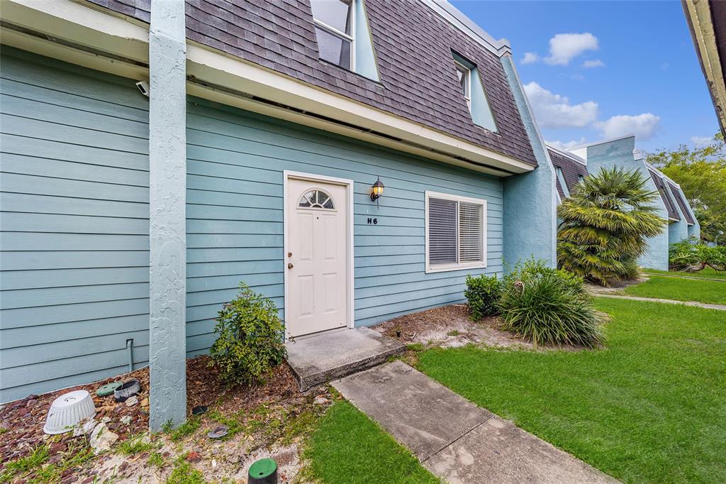 A blue-sided townhouse exterior features a white front door labeled H6 and a shingled roof — 501 SW 75TH STREET UNIT H6, GAINESVILLE, FL