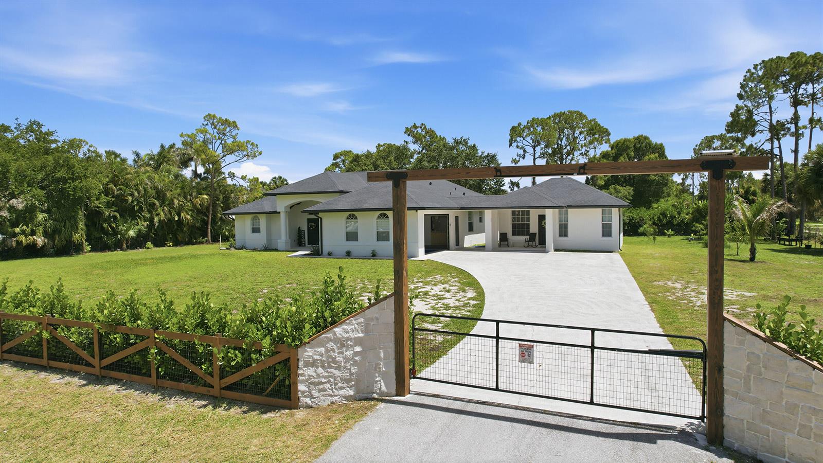 A white single-story house with a dark roof sits behind a gated concrete driveway — 18220 N 90th St Street N, FL 33470, FL