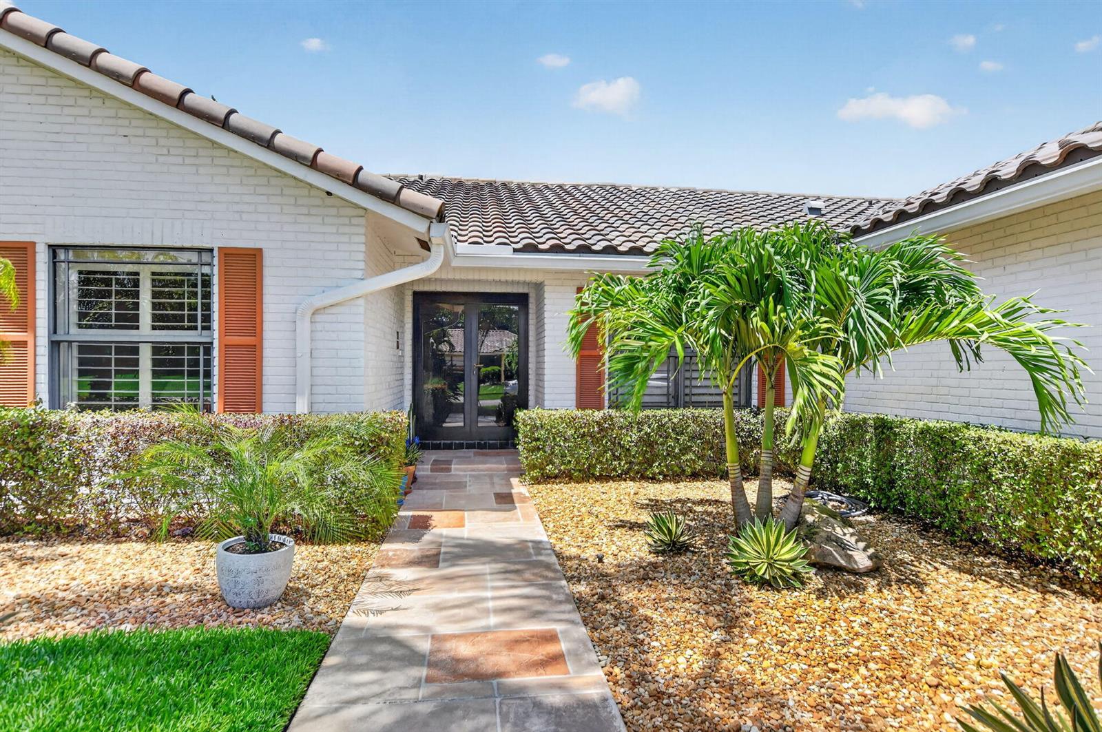 A white brick house exterior features a stone walkway leading to a dark glass front door — 10221 Harbourtown Court, Boca Raton FL 33498, BOCA RATON, FL