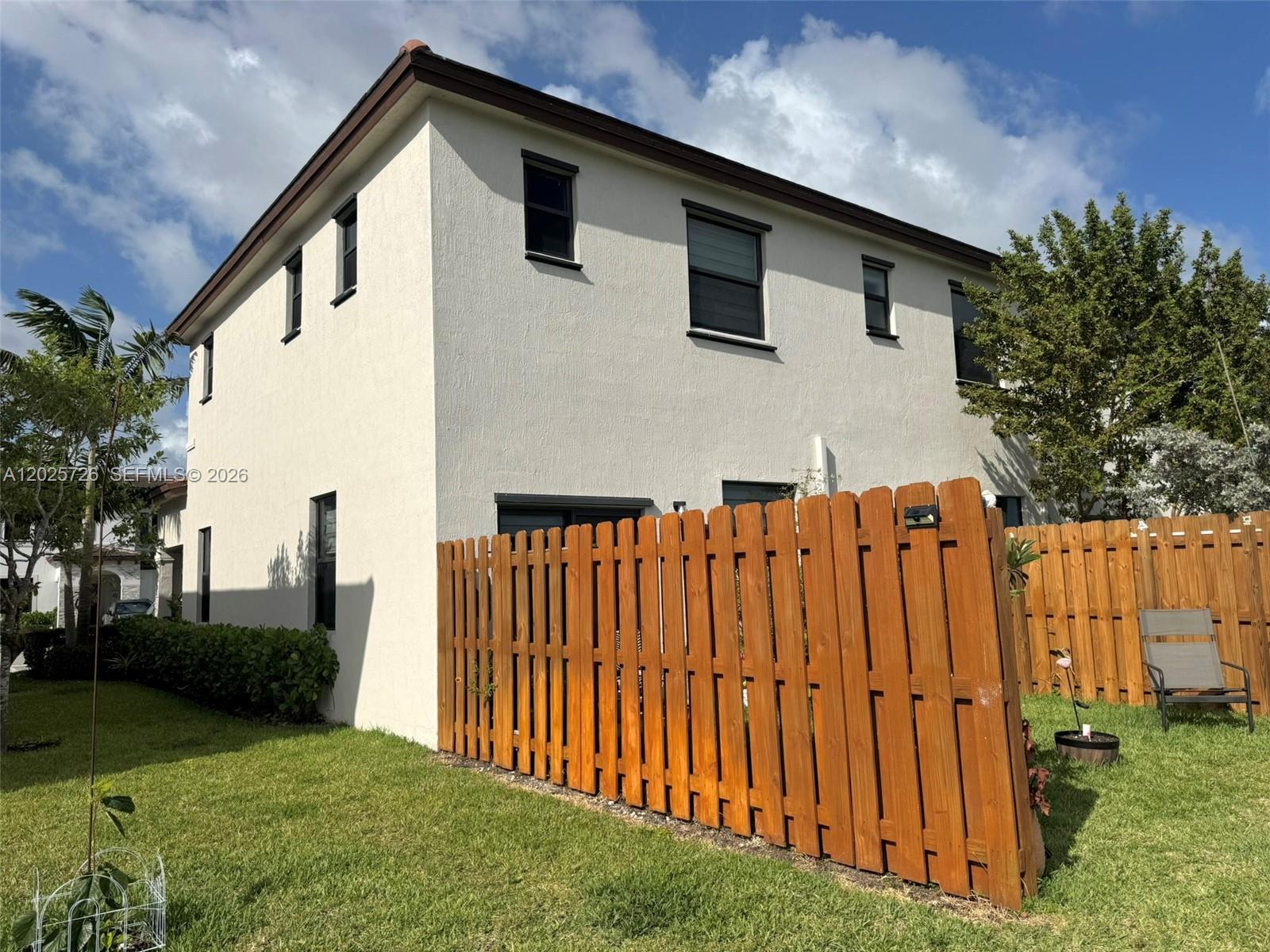 A two-story stucco house exterior features dark-framed windows and a wooden privacy fence — 10020 SW 228th Ter, Miami FL 33190, MIAMI, FL
