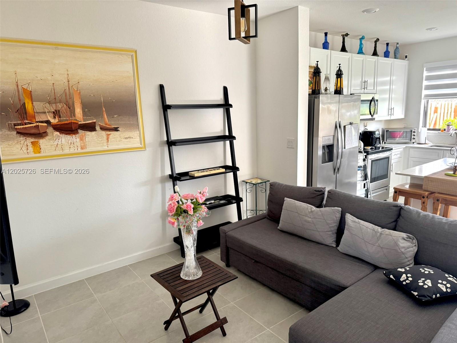 A living room with a gray sectional sofa, a ladder shelf, and an open kitchen — 10020 SW 228th Ter, Miami FL 33190, MIAMI, FL