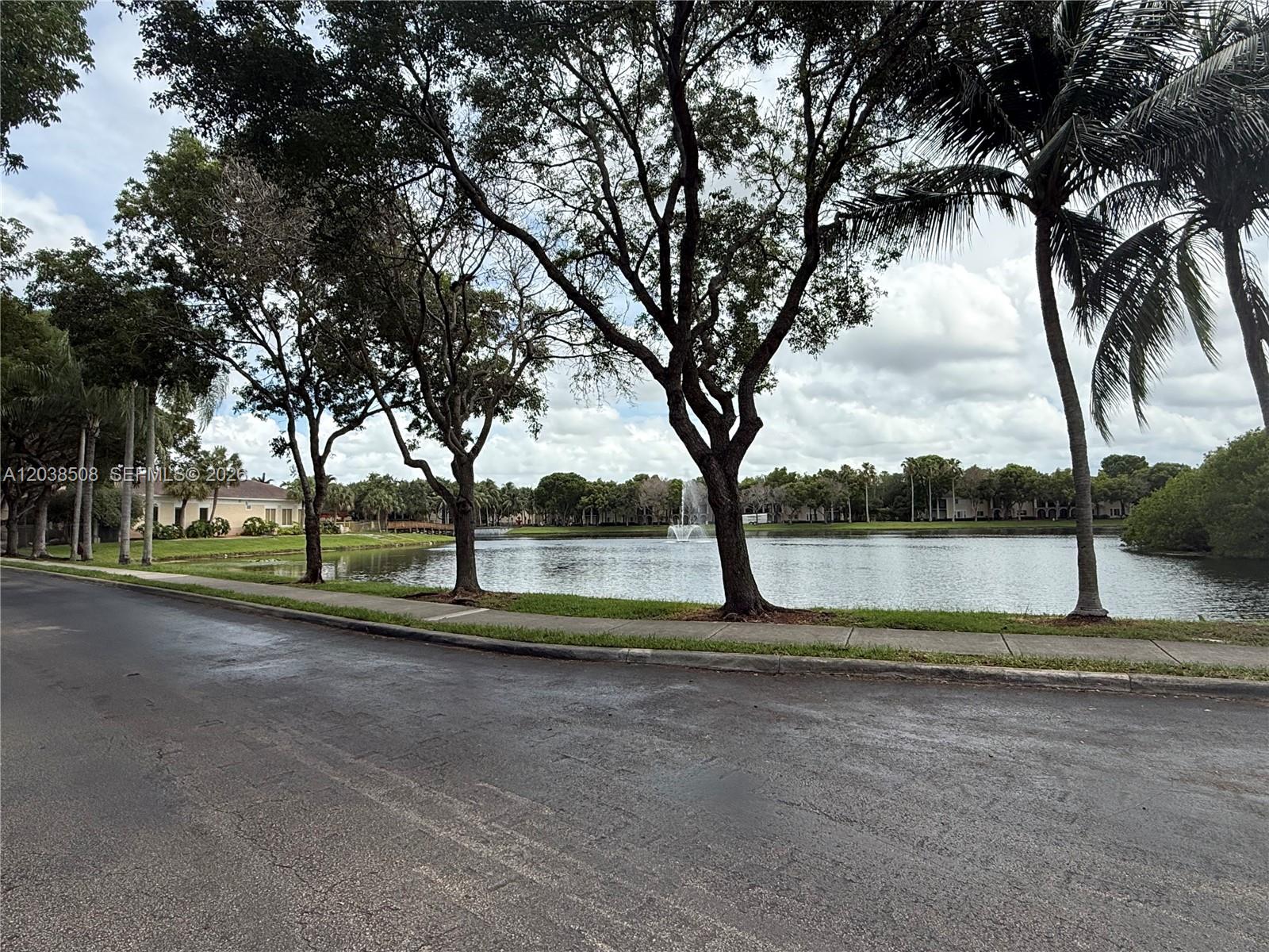 A paved road runs alongside a lake with a fountain and several mature trees — 2442 Centergate Dr # 206, Miramar FL 33025, MIRAMAR, FL