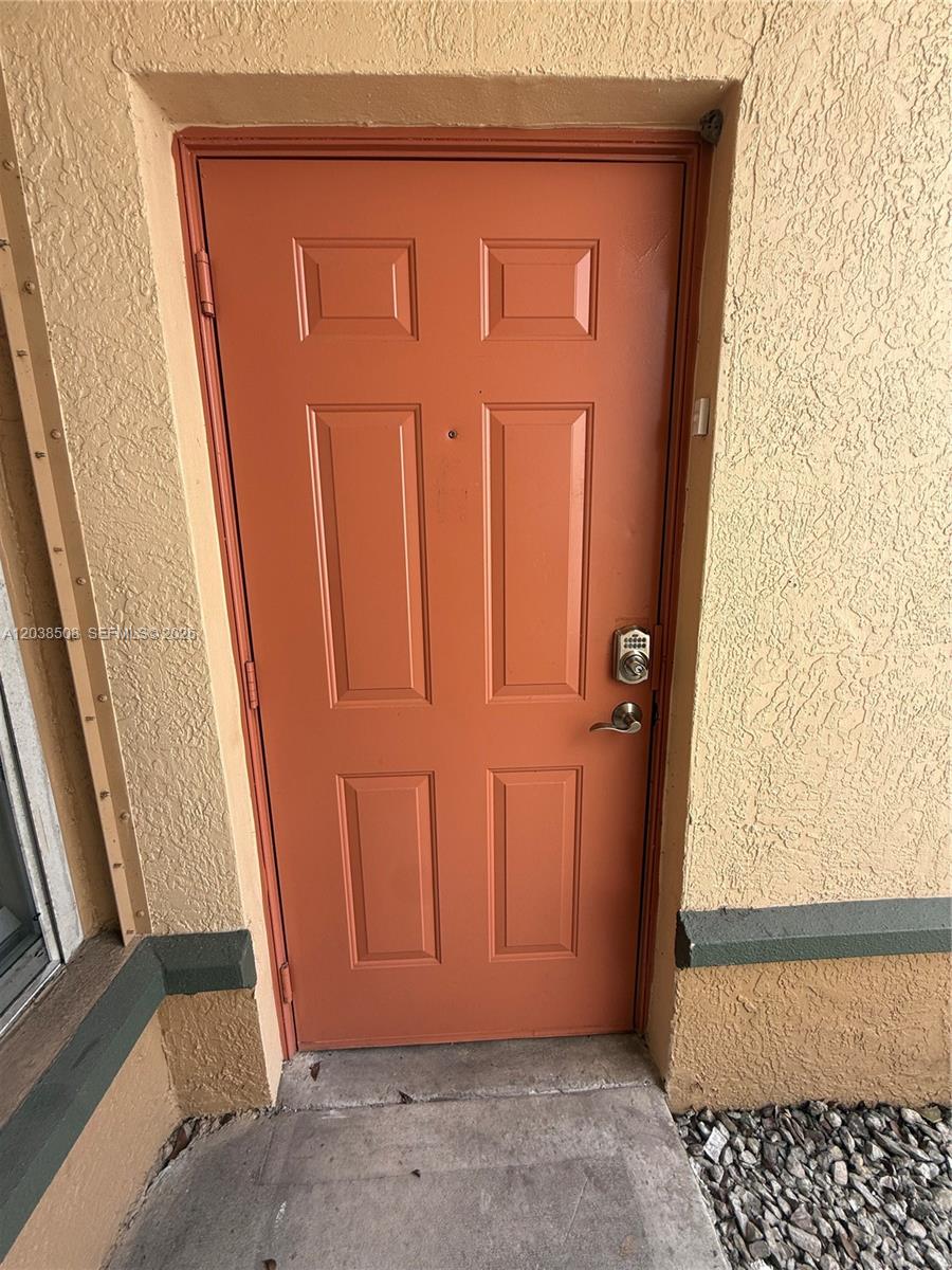 A terracotta-colored, four-panel front door with a keypad lock is set in a stucco wall — 2442 Centergate Dr # 206, Miramar FL 33025, MIRAMAR, FL