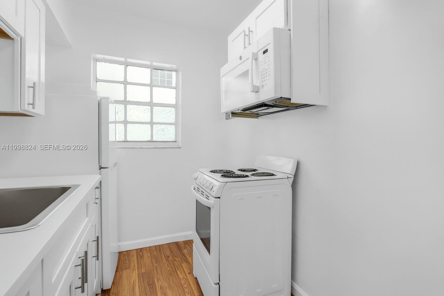 A small kitchen features white cabinets, a white stove, a microwave, and wood-look flooring — 635 8th St # 205, Miami Beach FL 33139, MIAMI BEACH, FL