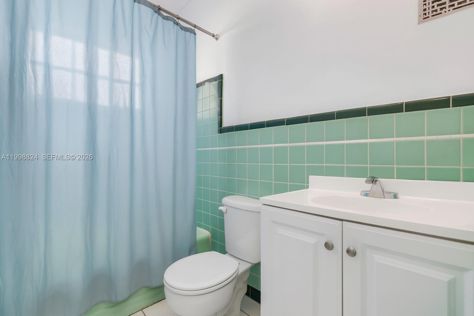 A bathroom features a white vanity, a toilet, and green tiled walls with a shower curtain — 635 8th St # 205, Miami Beach FL 33139, MIAMI BEACH, FL