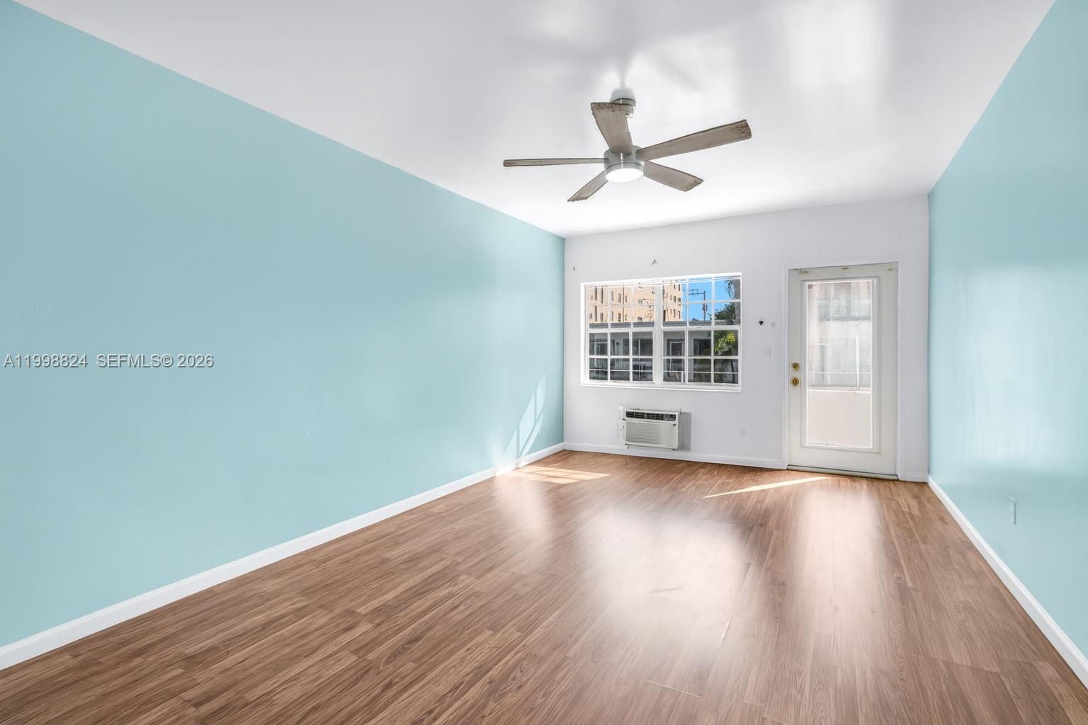 An empty room features light blue walls, wood-look flooring, a ceiling fan, and a window — 635 8th St # 205, Miami Beach FL 33139, MIAMI BEACH, FL