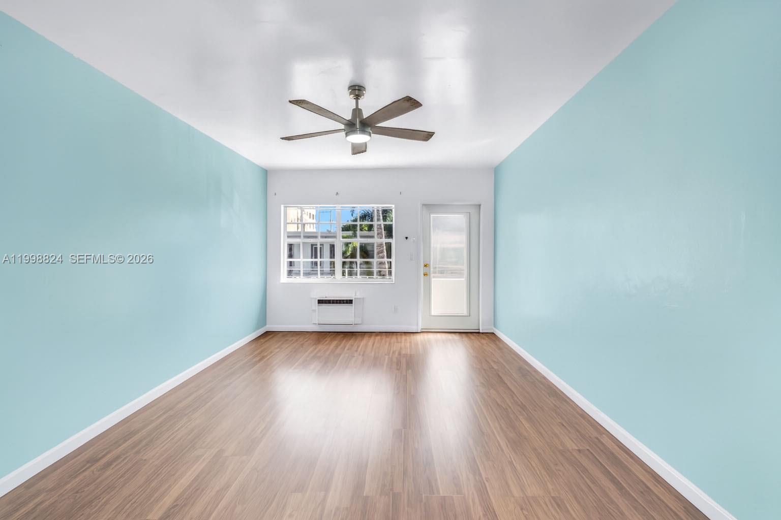 An empty room features light blue walls, wood-look flooring, a ceiling fan, and a window — 635 8th St # 205, Miami Beach FL 33139, MIAMI BEACH, FL