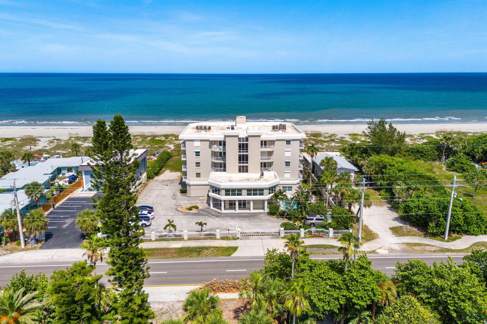 An aerial view shows a multi-story beachfront building with a parking lot and surrounding vegetation — 1155 S Atlantic Avenue # 203, Cocoa Beach FL 32931, COCOA BEACH, FL