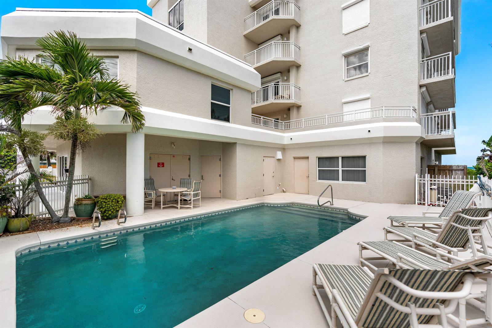 An outdoor swimming pool with lounge chairs sits beside a multi-story building with balconies — 1155 S Atlantic Avenue # 203, Cocoa Beach FL 32931, COCOA BEACH, FL
